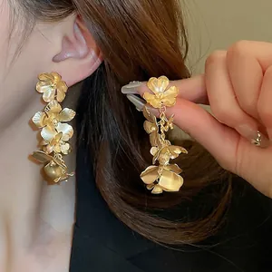 Elegant gold-tone layered flower drop earrings with a matte metallic finish on a model