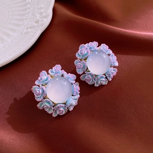 Macro detail of gradient blue rose earrings on dark brown silk fabric with flower petals