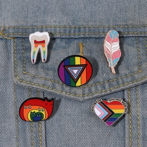 Fünf LGBTQ+ Emaille-Pins Set mit Regenbogen-Herz und Zähnen auf blauem Denim-Stoff