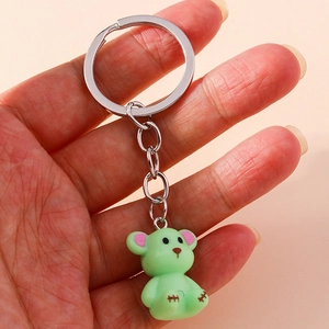 Close-up of a light green bear keychain with pink glitter ears and silver hardware
