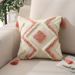 Detail of bohemian tufted cushion cover with orange diamond patterns and corner tassels