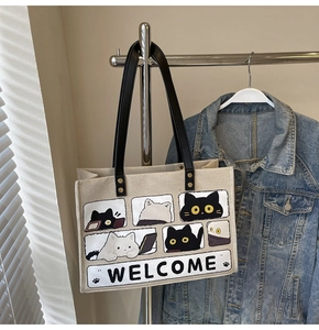 Close-up of beige canvas tote bag with cute cartoon cat illustrations and Welcome text