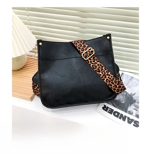 Close-up of black leather crossbody bag featuring a stylish leopard print wide strap