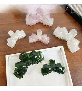 Close-up of acetate bow hair clips in green and cream on a wooden desk background