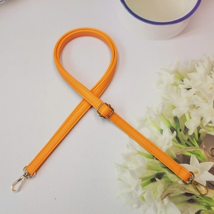 Détail de la bandoulière réglable en cuir litchi orange avec boucles dorées en métal