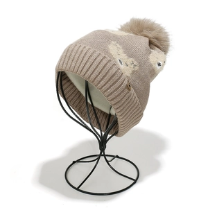 Detail der beigen Strickmütze mit flauschigem Bommel und süßem Bärenmuster-Gewebe