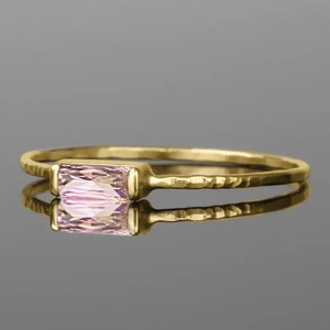 Detail of a thin gold ring featuring a hammered texture and a pink baguette gemstone