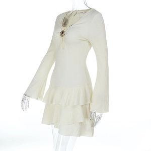 Détail de robe blanc cassé à col en V avec broche en métal et tissu texturé multicouche
