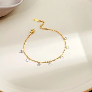 Detailed shot of gold bracelet with seven claw-set cubic zirconia charms on white ceramic