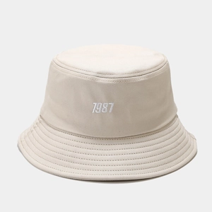 Detailed close-up of 1987 embroidery on a beige cotton bucket hat with stitched brim