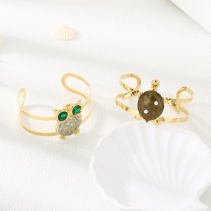 Golden owl and turtle open bangles with green crystals and pearls on white textured surface