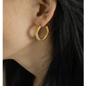 Close-up of a model wearing a golden twisted geometric hoop earring with high metal texture