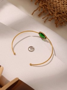 Macro shot of minimalist gold open bangle with a marquise-cut green gemstone setting