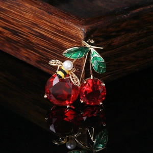 Macro detail of cherry brooch with red gemstones, green enamel leaves and pearl bee