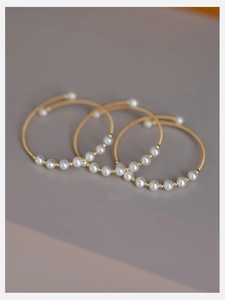 Detailed view of three minimalist gold-wire bangles featuring white pearls and gold beads