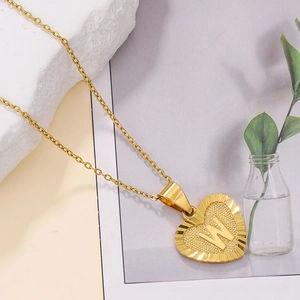 Detail of a gold heart pendant with letter W engraving and textured sunburst border