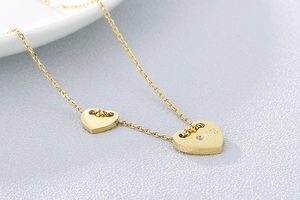 Makroaufnahme einer goldenen Herzkette mit LOVE Gravur und kleinem Kristallanhänger