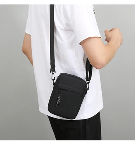 Detail of black nylon shoulder bag showing adjustable strap and decorative zipper pulls