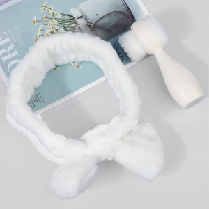 Close-up of a white plush bow headband and double-sided silicone facial cleansing brush