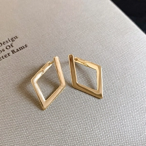Detailed view of geometric diamond-shaped gold earrings on a grey textured background