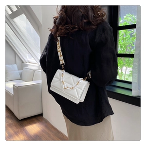 Close-up of white quilted crossbody bag with chunky chain and pattern wide strap