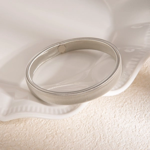 Gros plan d'un bracelet spiralé argenté texturé sur un plateau en céramique blanc