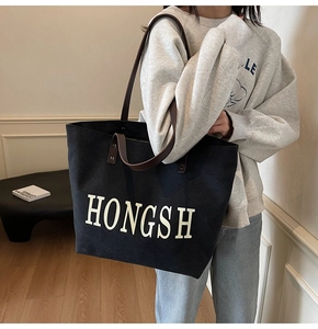 Large black canvas tote bag with brown leather straps shown worn on shoulder