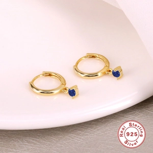 Close-up of gold S925 sterling silver hoop earrings with blue zircon drop on ceramic tray