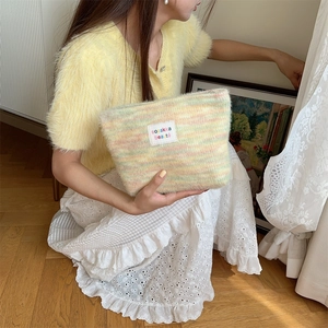Detail of plush rainbow striped makeup bag with zipper and textile label in hand
