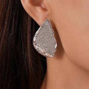 Close-up of a silver irregular geometric earring with a hammered crinkle metal texture