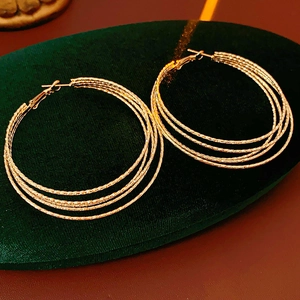 Close-up of golden multi-layer textured hoop earrings on green velvet cushion