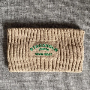 Detaillierte Strickstruktur des beigen Stirnbands mit grüner Stockholm-Stickerei