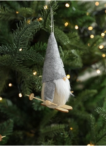 Felt Christmas gnome ornament hanging on a tree with wooden skis and warm light