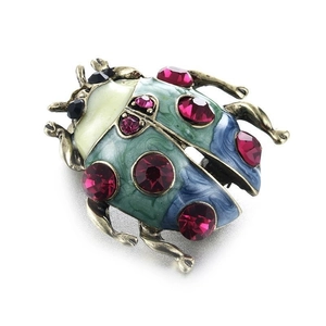 Macro shot of ladybug brooch featuring green enamel wings and red faceted gemstones
