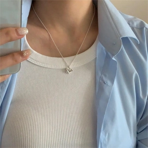 Close-up of minimalist 925 sterling silver heart necklace worn on a model with blue shirt