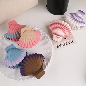 Flat lay of six matte scallop hair claws with pastel gradient colors on a ceramic tray