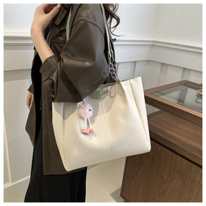 Dettaglio di una grande borsa tote crema con manici verdi e ciondolo pompon rosa sul modello
