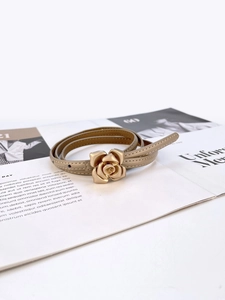 Detail of khaki leather belt featuring a golden rose-shaped buckle on a magazine background