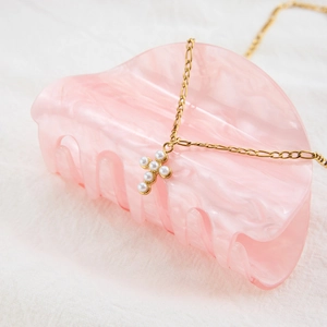 Detail of a gold cross pearl necklace displayed on a pink marble hair claw clip