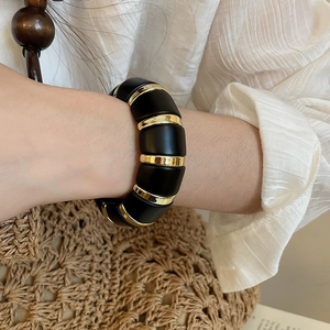 Close-up of matte black acrylic and gold metal link bracelet on a woman wrist