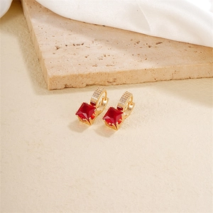Close-up of gold square earrings with deep red gemstones and pavé clear zircon accents