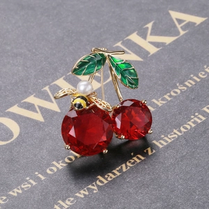 Close-up of cherry brooch with red gemstone fruits, green leaves and a small pearl bee
