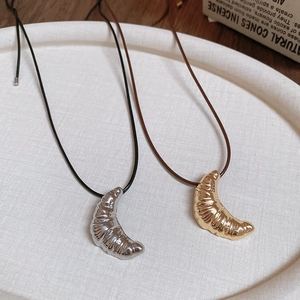 Close-up of croissant pendants in gold and silver with textured metal on leather cords