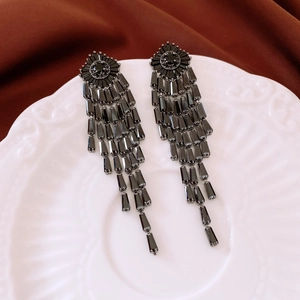 Detail view of vintage fringe earrings with black crystals on a white ceramic plate