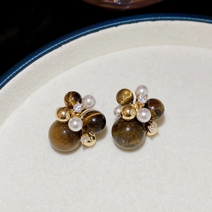 Close-up of cluster earrings with tiger eye stone, pearl and zircon in gold setting