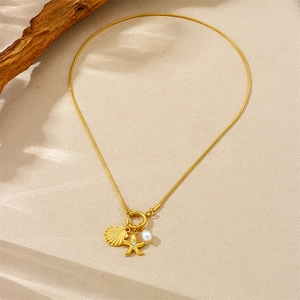 Gold starfish seashell and pearl charm necklace on beach sand with rustic wood