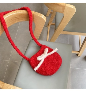 Detail of red plush crossbody bag featuring a white fuzzy bow on a wooden chair