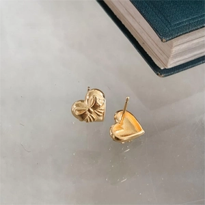 Macro detail of golden heart stud earrings with delicate bow relief on marble background
