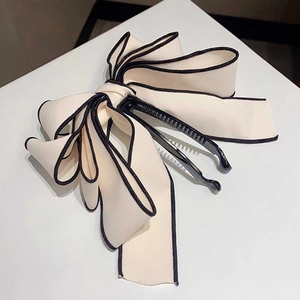 Detailed close-up of a beige fabric bow hair clip with distinctive black edge detailing