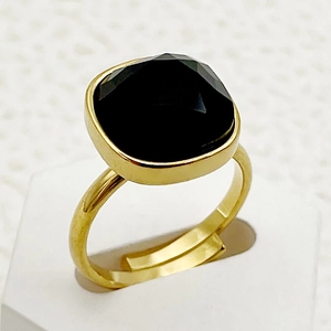 Gros plan d'une bague dorée ornée d'un zircon noir carré sur un support d'exposition blanc